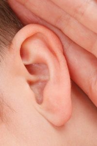 Image of a man holding his hand up to his ear, to listen more closely to something.