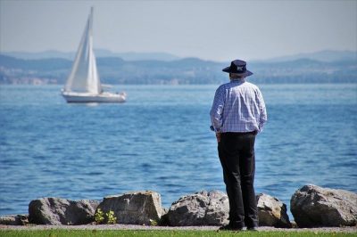 Man looking out over water at a sailboat going by.